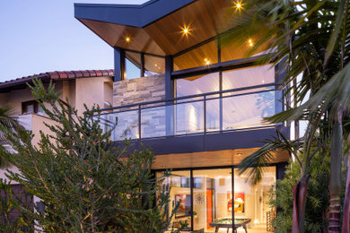 Inspiration for a large mid-century modern gray three-story stone house exterior remodel in Los Angeles with a butterfly roof, a metal roof and a black roof