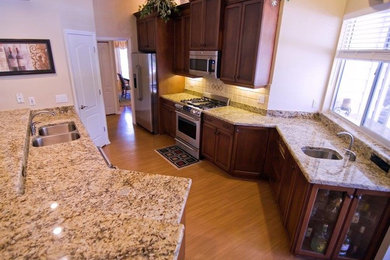 Elegant u-shaped light wood floor open concept kitchen photo in Jacksonville with an undermount sink, shaker cabinets, medium tone wood cabinets, granite countertops, beige backsplash, ceramic backsplash, stainless steel appliances and an island