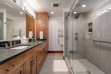 Contemporary bathroom in Seattle with shaker cabinets, brown cabinets, a double shower, beige tile, porcelain tile, white walls, porcelain floors, an undermount sink, granite benchtops, beige floor, a sliding shower screen and black benchtops.