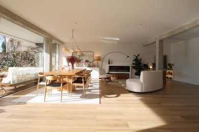 Foto de comedor ecléctico abierto con paredes blancas, suelo de madera clara y chimenea lineal