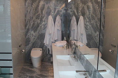 Example of a large trendy master gray tile and porcelain tile marble floor and gray floor bathroom design in New York with flat-panel cabinets, black cabinets, a one-piece toilet, multicolored walls, a wall-mount sink, quartz countertops and a hinged shower door