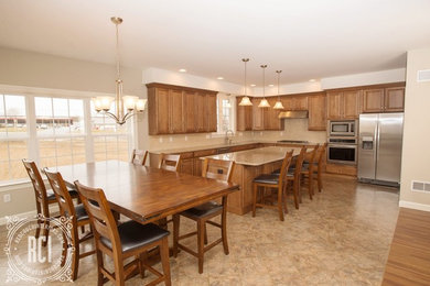 Large elegant l-shaped vinyl floor eat-in kitchen photo with an undermount sink, raised-panel cabinets, medium tone wood cabinets, granite countertops, beige backsplash, porcelain backsplash, stainless steel appliances and an island