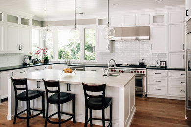 Design ideas for a mid-sized transitional u-shaped eat-in kitchen in San Francisco with a farmhouse sink, shaker cabinets, white cabinets, quartzite benchtops, white splashback, stainless steel appliances, medium hardwood floors, with island, brown floor, black benchtop and subway tile splashback.