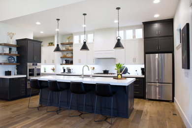 Example of a transitional light wood floor kitchen design in Other with an undermount sink, shaker cabinets, black cabinets, quartzite countertops, white backsplash, ceramic backsplash, stainless steel appliances and white countertops
