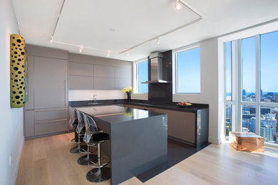 Inspiration for a mid-sized modern l-shaped light wood floor and beige floor kitchen remodel in New York with an undermount sink, flat-panel cabinets, gray cabinets, gray backsplash, stone slab backsplash, paneled appliances, an island and gray countertops