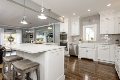 Inspiration for a mid-sized traditional l-shaped eat-in kitchen in New York with a farmhouse sink, recessed-panel cabinets, white cabinets, quartz benchtops, grey splashback, stainless steel appliances, dark hardwood floors, with island, brown floor and white benchtop.