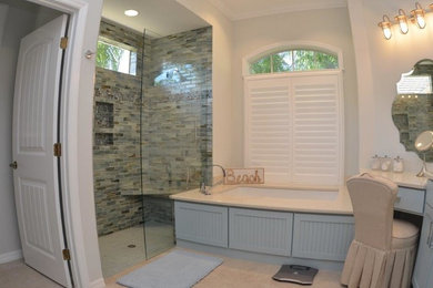 Example of a mid-sized beach style master beige tile, brown tile, gray tile, multicolored tile and stone tile travertine floor doorless shower design in Orange County with shaker cabinets, blue cabinets, an undermount tub, a one-piece toilet, beige walls and limestone countertops