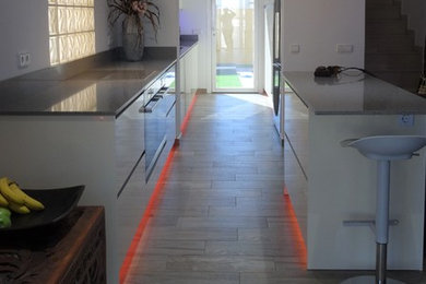 Diseño de cocina lineal minimalista abierta con fregadero bajoencimera, armarios con paneles lisos, encimera de cuarzo compacto, electrodomésticos de acero inoxidable, una isla y encimeras grises