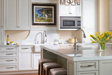 Design ideas for a beach style l-shaped separate kitchen in Atlanta with a farmhouse sink, recessed-panel cabinets, white cabinets, marble benchtops, white splashback, marble splashback, medium hardwood floors, with island, brown floor and white benchtop.