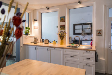 Immagine di un grande cucina con isola centrale con lavello sottopiano, ante bianche, top in legno, paraspruzzi grigio, elettrodomestici da incasso e pavimento grigio