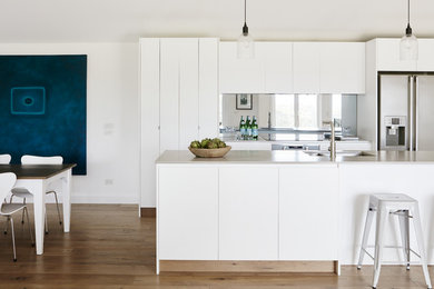 Design ideas for a large contemporary galley eat-in kitchen in Sydney with an undermount sink, flat-panel cabinets, white cabinets, concrete benchtops, metallic splashback, mirror splashback, stainless steel appliances, medium hardwood floors and with island.