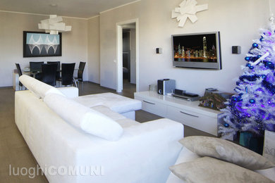 Modelo de sala de estar abierta moderna de tamaño medio con paredes blancas, suelo de baldosas de porcelana y televisor colgado en la pared