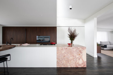 Photo of a large contemporary galley open plan kitchen in Sydney with a double-bowl sink, flat-panel cabinets, white cabinets, solid surface benchtops, black appliances, dark hardwood floors, with island and white benchtop.