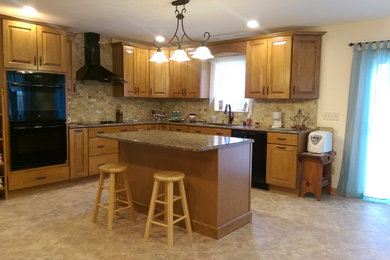 Inspiration for a large timeless l-shaped vinyl floor eat-in kitchen remodel in Philadelphia with an undermount sink, raised-panel cabinets, medium tone wood cabinets, granite countertops, multicolored backsplash, stone tile backsplash, black appliances and an island