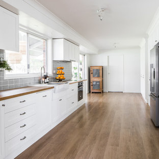 Inspiration for a mid-sized country galley kitchen pantry in Sydney with shaker cabinets, white cabinets, wood benchtops, grey splashback, subway tile splashback, stainless steel appliances, painted wood floors and brown floor.
