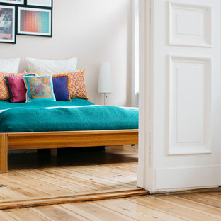 Cette photo montre une chambre parentale tendance de taille moyenne avec un mur blanc, un sol en bois clair, un sol marron et cheminée suspendue.