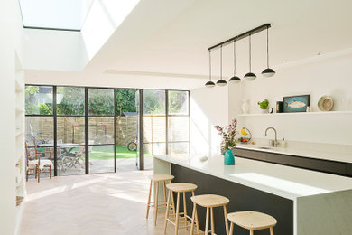 This is an example of a large contemporary single-wall open plan kitchen in London with flat-panel cabinets, black cabinets, quartzite benchtops, white splashback, with island and grey benchtop.