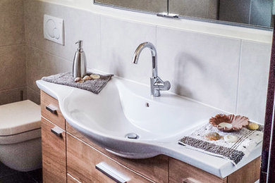 Mittelgroßes Modernes Badezimmer En Suite mit Kassettenfronten, dunklen Holzschränken, bodengleicher Dusche, Wandtoilette mit Spülkasten, grauen Fliesen, Keramikfliesen, beiger Wandfarbe, Keramikboden, Aufsatzwaschbecken, Mineralwerkstoff-Waschtisch, schwarzem Boden, offener Dusche und weißer Waschtischplatte in Dortmund