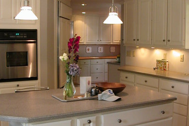 Mid-sized elegant single-wall medium tone wood floor and brown floor enclosed kitchen photo in Orange County with an undermount sink, raised-panel cabinets, white cabinets, laminate countertops, stainless steel appliances and an island