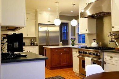 Inspiration for a large timeless medium tone wood floor and brown floor kitchen remodel in New York with a farmhouse sink, recessed-panel cabinets, white cabinets, soapstone countertops, white backsplash, ceramic backsplash, stainless steel appliances, an island and black countertops