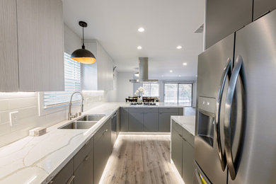 Example of a mid-sized minimalist l-shaped vinyl floor and gray floor open concept kitchen design in Los Angeles with a double-bowl sink, flat-panel cabinets, gray cabinets, quartzite countertops, white backsplash, ceramic backsplash, stainless steel appliances, a peninsula and white countertops
