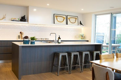 Photo of a contemporary galley kitchen in Sydney with a double-bowl sink, flat-panel cabinets, dark wood cabinets, solid surface benchtops, white splashback, subway tile splashback, stainless steel appliances, medium hardwood floors and with island.