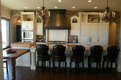 Example of a large mountain style single-wall dark wood floor eat-in kitchen design in Denver with raised-panel cabinets, an island, white cabinets, wood countertops, paneled appliances, gray backsplash, brick backsplash and a farmhouse sink