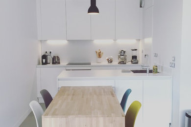 Photo of a small modern galley eat-in kitchen in Montpellier with a single-bowl sink, flat-panel cabinets, white cabinets, laminate benchtops, white splashback, stainless steel appliances and with island.