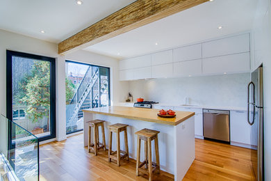 Inspiration for a modern kitchen in Montreal with white cabinets, white splashback, light hardwood floors, with island, brown floor and white benchtop.