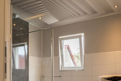 Photo of a mid-sized contemporary 3/4 bathroom in Leipzig with an open shower, flat-panel cabinets, white cabinets, a curbless shower, a two-piece toilet, white tile, ceramic tile, grey walls, ceramic floors, an integrated sink, solid surface benchtops, grey floor and white benchtops.
