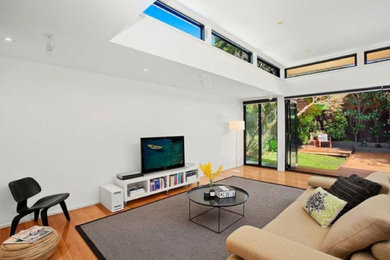 Modelo de salón abierto actual de tamaño medio con paredes blancas, suelo de madera clara y televisor independiente