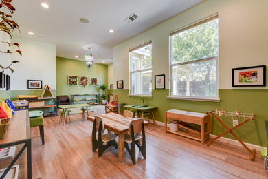 Diseño de habitación infantil unisex de 1 a 3 años actual de tamaño medio con escritorio, paredes verdes, suelo de madera en tonos medios y suelo marrón