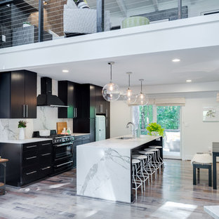 Diseño de cocina de galera, actual, grande, abierta, con fregadero bajoencimera, una isla, armarios con paneles lisos, puertas de armario negras, encimera de mármol, salpicadero verde, salpicadero de losas de piedra, electrodomésticos de acero inoxidable y suelo de madera clara