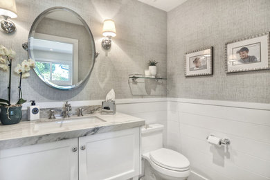 Inspiration for a mid-sized transitional powder room in Orange County with recessed-panel cabinets, white cabinets, a one-piece toilet, grey walls, an undermount sink and granite benchtops.