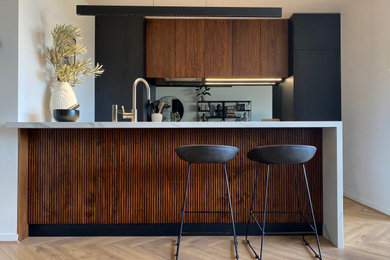 Mid-sized contemporary single-wall open plan kitchen in Melbourne with a drop-in sink, raised-panel cabinets, dark wood cabinets, quartz benchtops, grey splashback, mirror splashback, stainless steel appliances, laminate floors, a peninsula and white benchtop.