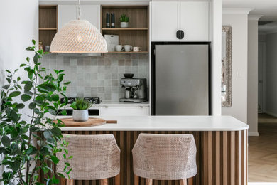 Mid-sized mediterranean open plan kitchen in Sydney with a drop-in sink, shaker cabinets, white cabinets, quartz benchtops, multi-coloured splashback, ceramic splashback, black appliances, light hardwood floors, with island, beige floor and grey benchtop.