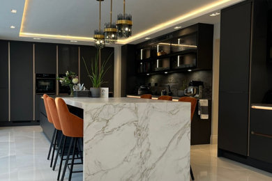 Inspiration for a large grey and black l-shaped kitchen/diner in London with a submerged sink, flat-panel cabinets, black cabinets, black splashback, black appliances, an island, grey floors and black worktops.