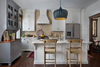 Example of a small classic l-shaped dark wood floor and brown floor kitchen design in Detroit with a farmhouse sink, shaker cabinets, white cabinets, marble countertops, beige backsplash, mosaic tile backsplash, stainless steel appliances and an island