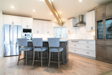 Beach style light wood floor, beige floor and exposed beam open concept kitchen photo in San Francisco with an undermount sink, shaker cabinets, white cabinets, quartz countertops, white backsplash, ceramic backsplash, stainless steel appliances, an island and white countertops