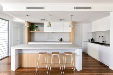 Inspiration for a large scandinavian l-shaped eat-in kitchen in Perth with a double-bowl sink, flat-panel cabinets, white cabinets, quartz benchtops, grey splashback, engineered quartz splashback, black appliances, medium hardwood floors, with island, brown floor and grey benchtop.