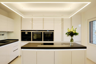 Mittelgroße Moderne Küche in L-Form mit integriertem Waschbecken, flächenbündigen Schrankfronten, weißen Schränken, Küchenrückwand in Weiß, Glasrückwand, Küchengeräten aus Edelstahl und Kücheninsel in Berlin