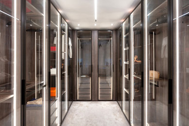 Medium sized modern gender neutral walk-in wardrobe in London with glass-front cabinets, dark wood cabinets, carpet, beige floors and feature lighting.