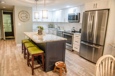 Mid-sized beach style l-shaped medium tone wood floor and brown floor eat-in kitchen photo in Other with an undermount sink, shaker cabinets, white cabinets, granite countertops, white backsplash, subway tile backsplash, stainless steel appliances, an island and multicolored countertops