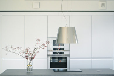 Offene, Mittelgroße Moderne Küche in L-Form mit flächenbündigen Schrankfronten, weißen Schränken, Laminat-Arbeitsplatte, Küchenrückwand in Weiß, weißen Elektrogeräten, dunklem Holzboden, Kücheninsel, grauem Boden und grauer Arbeitsplatte in Hamburg