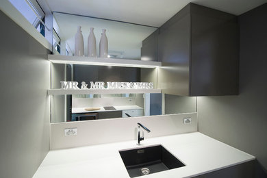Photo of a small contemporary galley separate kitchen in Sydney with a single-bowl sink, flat-panel cabinets, solid surface benchtops, mirror splashback, light hardwood floors and no island.