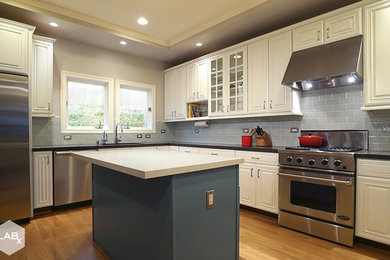 Mid-sized transitional u-shaped medium tone wood floor enclosed kitchen photo in San Francisco with an undermount sink, raised-panel cabinets, white cabinets, quartz countertops, blue backsplash, ceramic backsplash, stainless steel appliances and an island
