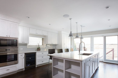 Inspiration for a large transitional galley dark wood floor kitchen remodel in Chicago with an undermount sink, shaker cabinets, white cabinets, quartzite countertops, white backsplash, glass tile backsplash, stainless steel appliances and an island