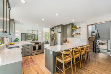 Example of a danish l-shaped light wood floor eat-in kitchen design in Denver with a single-bowl sink, shaker cabinets, green cabinets, quartz countertops, white backsplash, ceramic backsplash, stainless steel appliances, a peninsula and white countertops