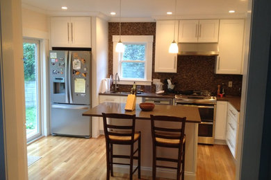 This is an example of a mid-sized traditional l-shaped eat-in kitchen in Boston with an undermount sink, shaker cabinets, white cabinets, solid surface benchtops, brown splashback, stone tile splashback, stainless steel appliances, light hardwood floors, with island, beige floor and brown benchtop.
