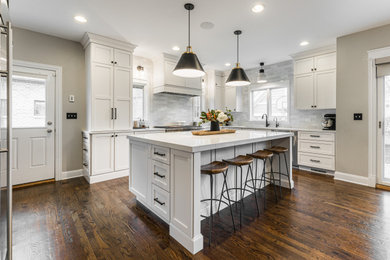 Large transitional l-shaped dark wood floor and brown floor open concept kitchen photo in Chicago with an undermount sink, shaker cabinets, white cabinets, quartz countertops, white backsplash, ceramic backsplash, stainless steel appliances, an island and white countertops